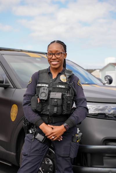Lakewood Police Officer Lesha Cockle stands in front of her patrol vehicle, smiling at the camera.